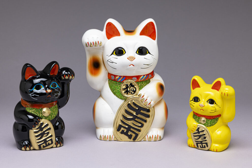 Maneki-neko; Puppenmanufaktur Baigetsu Tomimoto-Ningyoen Tokoname, Präfektur Aichi, Japan, 2025; Keramik (Ton), 16 x 11 x 10 cm (Schwarz :1); 23 x 16 x 15 cm (Weiß :2); 13 x 9 x 8 cm (Gelb :3) MARKK Inv Nrn. 2025.15:1-3, Ankauf, 2025.